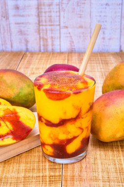 chamoyada or mango smoothie with chamoy and a bamboo straw, a refreshing mexican drink. served with mangoes and chamoy on a wooden table with a white wooden plank backdrop. clipart