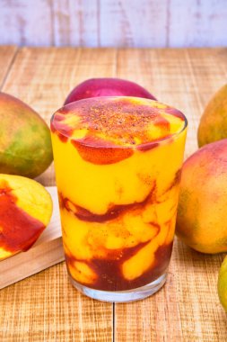 Chamoyada veya chamoy ile mango smoothie, Meksika ferahlatıcı bir içecek. Ahşap bir masada beyaz ahşap arka planda mangolarla servis edilir..
