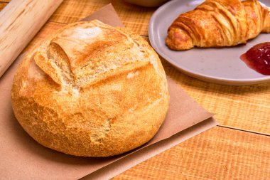 Kahverengi tabakta yuvarlak Fransız ekmeği ve yanında reçelli kruvasan, kırsal yemek kavramı..