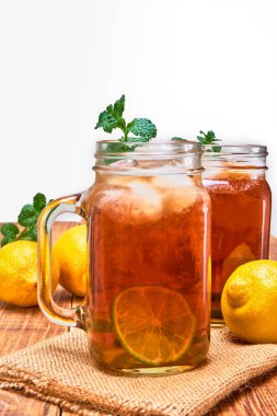 Buzlu siyah çay, bir dilim limon ve buzlu küp ve üzerinde nane yaprağı olsun. Yanında zencefil, limonlu Eureka ve tahta bir masa ve beyaz bir arka plan üzerinde nane yaprakları. Boşluğu kopyala