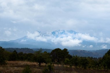 Puebla şehrinin dağları, Meksika ön planda orman çalıları ve bir sürü bulutla dolu dramatik bir gökyüzü ile yeni kar yağdı..
