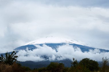 Meksika 'nın Puebla şehrindeki volkan, diplerinde orman ağaçları ile taze kar yağdı. Bir sürü bulutlu dramatik gökyüzü.