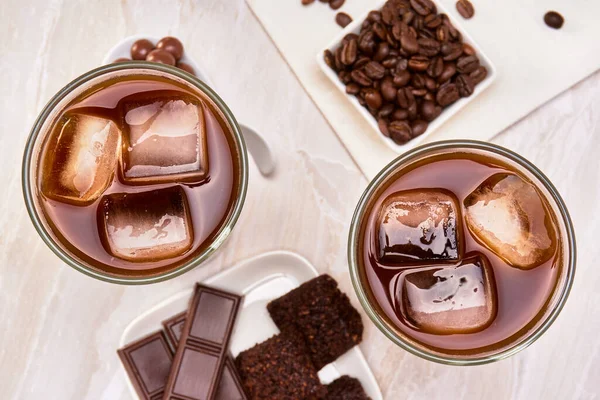 cold brew coffee accompanied by chocolate pearls, chocolate bars, vegan chocolate brownies and coffee beans on a marble surface copy space for advertising. top view. luxury concept.