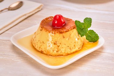 flan napolitano (mexican dessert) garnished with a cherry and a mint leaf on a white plate on a marble surface. copy space for advertising. elegant concept. clipart