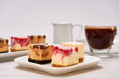 Üç New York peyniri, çikolata ve karamel, çilekli ve limonlu mini turta beyaz mermer bir tabakta ve beyaz arka planda. Reklam için kopyalama alanı. yatay