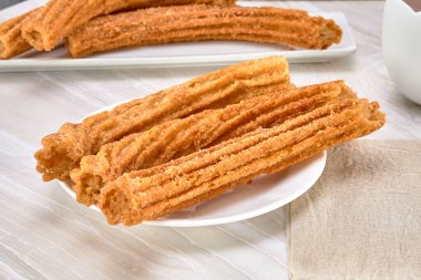 Beyaz bir tepside beyaz bir tabakta beyaz bir zeminde şeker ve tarçınla kaplı İspanyol churro 'ları ve beyaz arka plan. görünümü kapat.