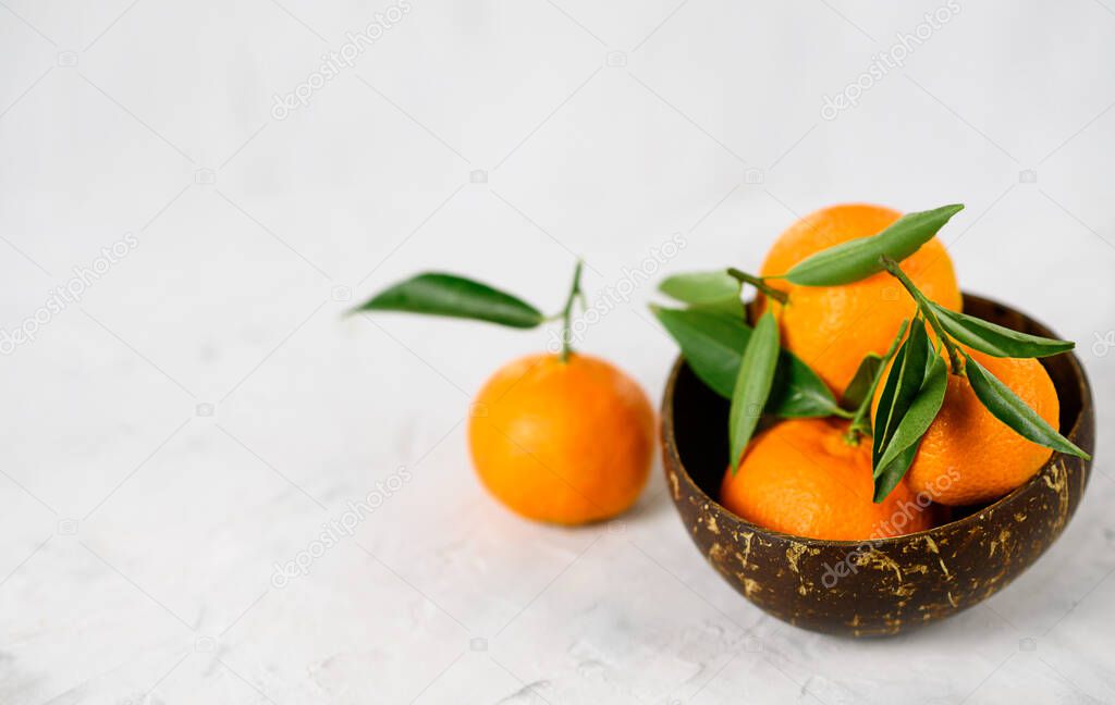 bowl with fresh citrus fruits standing on grey background . Mandarins, limes and sliced oranges with leaves laying on table. Side view. Nutrition and vegetarian concept.