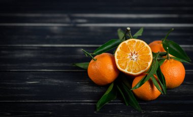 Siyah ahşap arka planda yaprakları olan Mandarinler.. 