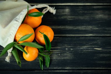 Taze mandarin narenciye meyveleri siyah ahşap arka planda eko torbada. Boşluğu kopyala.