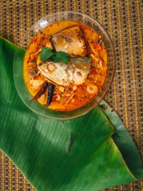 Baharatlı ve sıcak kral balığı körisinin ahşap masa üzerinde bitki ve biberli hali, Hindistan cevizi sütü ve yumurta pantolonlu yabani otlardan yapılmış Tayland yemeği, körili balık.