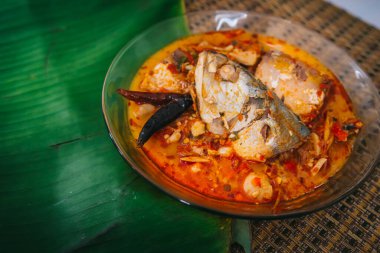 Baharatlı ve sıcak kral balığı körisinin ahşap masa üzerinde bitki ve biberli hali, Hindistan cevizi sütü ve yumurta pantolonlu yabani otlardan yapılmış Tayland yemeği, körili balık.