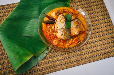 Baharatlı ve sıcak kral balığı körisinin ahşap masa üzerinde bitki ve biberli hali, Hindistan cevizi sütü ve yumurta pantolonlu yabani otlardan yapılmış Tayland yemeği, körili balık.