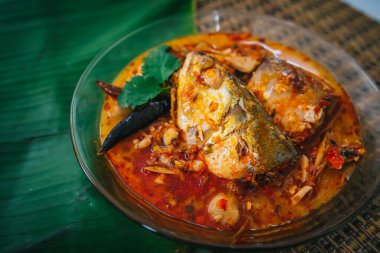 Baharatlı ve sıcak kral balığı körisinin ahşap masa üzerinde bitki ve biberli hali, Hindistan cevizi sütü ve yumurta pantolonlu yabani otlardan yapılmış Tayland yemeği, körili balık.