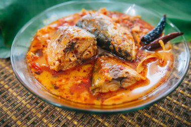 Baharatlı ve sıcak kral balığı körisinin ahşap masa üzerinde bitki ve biberli hali, Hindistan cevizi sütü ve yumurta pantolonlu yabani otlardan yapılmış Tayland yemeği, körili balık.