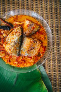 Baharatlı ve sıcak kral balığı körisinin ahşap masa üzerinde bitki ve biberli hali, Hindistan cevizi sütü ve yumurta pantolonlu yabani otlardan yapılmış Tayland yemeği, körili balık.