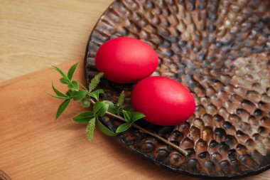 İki kırmızı paskalya yumurtası ve tabakta yeşil bir dal, ahşap masa. 