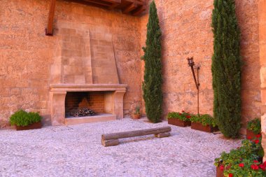 Şömineli tören alanı, ahşap bank, selvi ağaçları ve çiçek kutuları. Belmonte Ortaçağ Kalesi.