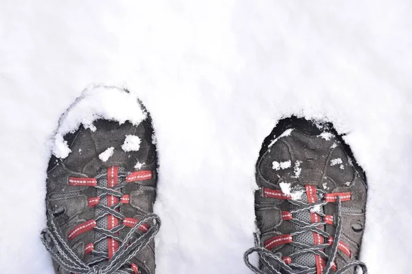 Feet in hiking boots stepping on the snow. Black, gray and red boots. Snow storm called Filomena. La Rioja, Spain.