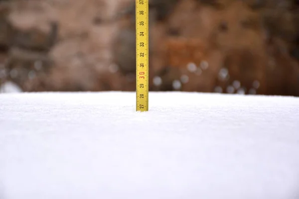 Yellow tape measure measuring snow cover after the storm. Filomena snow storm in La Rioja, Spain, January 2021.