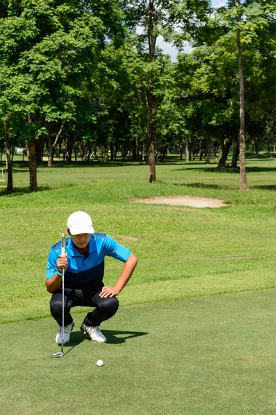Asiático joven se arrodilla, mira la pelota de golf, mientras que el golf . —  Fotos de Stock