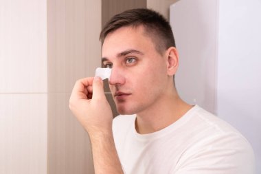 man puts on and removes a strip for the nose from black dots. Coal cleaning strips from blackheads and comedones. The concept of personal care clipart