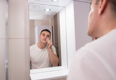 Adam banyoda yüzünü nemlendiriyor. Adam aynaya bakar ve yüzüne bakar..