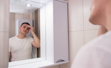 Adam banyoda yüzünü nemlendiriyor. Adam aynaya bakar ve yüzüne bakar..