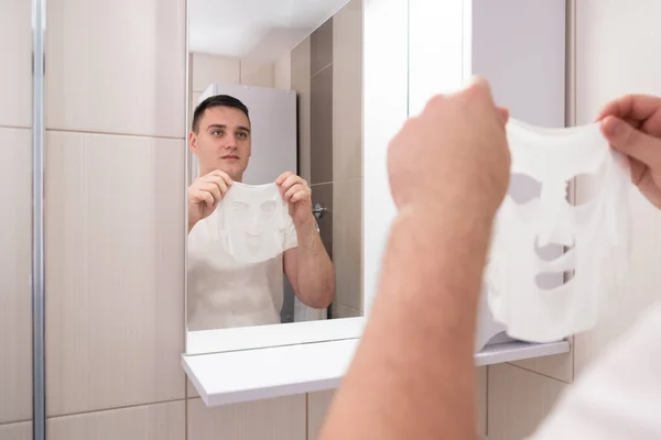 reflection in the mirror man takes care of his face. guy in the bathroom with a face mask.