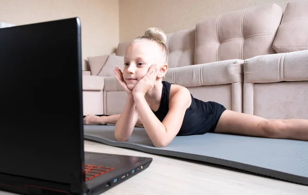 The child watches online video on a laptop and performs sports exercises - yoga, gymnastics. Stay at home. Self-isolation, quarantine, online education concept