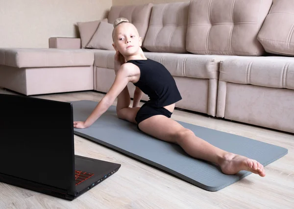 Çocuk dizüstü bilgisayarda video izliyor ve spor egzersizleri yapıyor. Yoga, jimnastik. Evde kal. Kişisel izolasyon, karantina, online eğitim kavramı