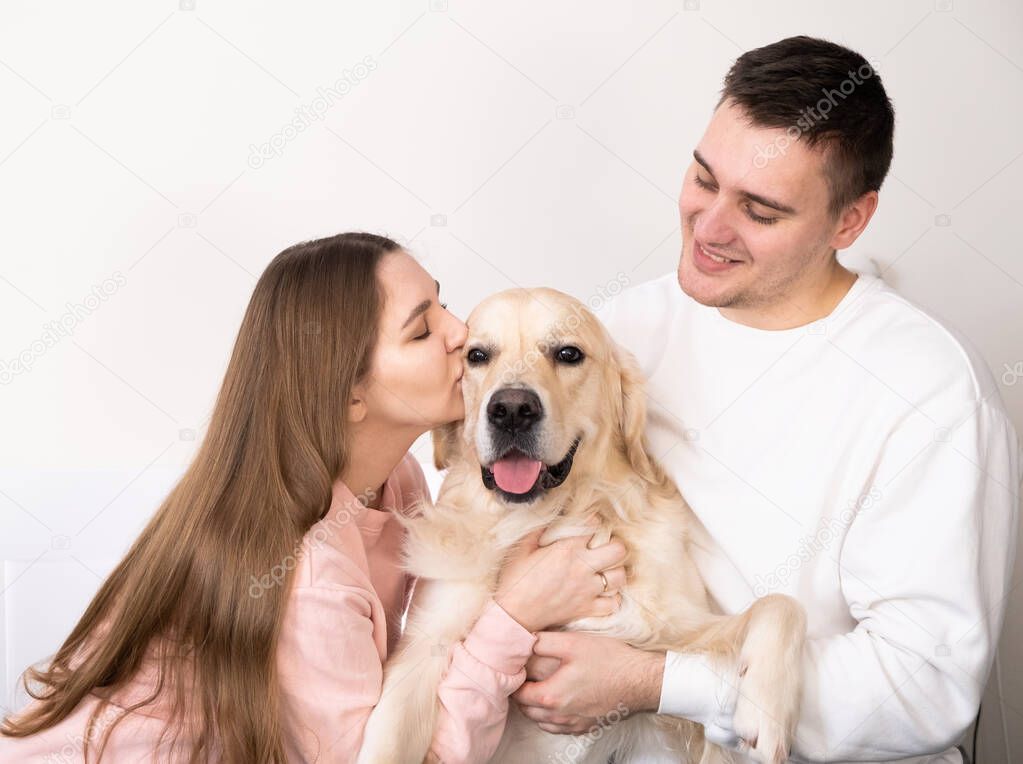 Happy family hugs the dog. A funny golden retriever in the arms of the owner. Husband and wife kiss and hug a pet.