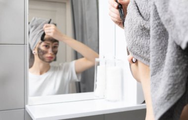 Deri bakımı konsepti. Genç kız banyo aynasının önünde yüzüne maske takıyor.