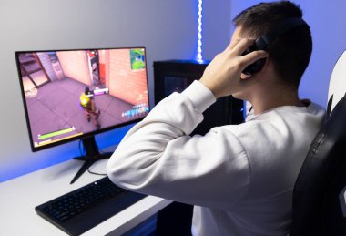 Adam online bir oyun oynuyor. Oyuncu mavi neon bir odada bilgisayarın başında oturuyor..