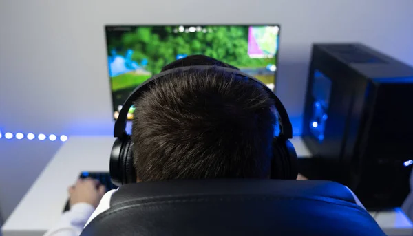 The guy is playing an online game. Gamer sits at a computer in a blue neon room.