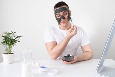 Bir erkek evde yüz derisine dikkat eder. Adam yüzüne kilden bir maske takıyor. Erkek sağlığı ve güzellik kavramı, kozmetoloji, vücut ve cilt bakımı.