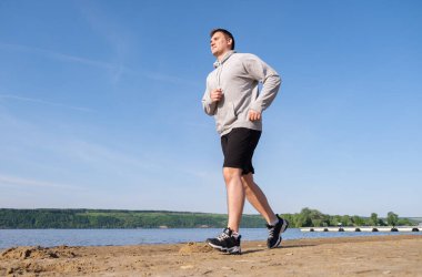Gri kazaklı genç bir adam gün doğumunda boş bir sahilde koşar. Zayıflama ve sağlıklı yaşam tarzı konsepti.