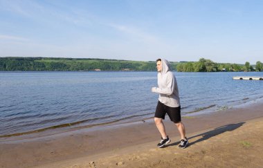 Gri kazaklı genç bir adam gün doğumunda boş bir sahilde koşar. Zayıflama ve sağlıklı yaşam tarzı konsepti.