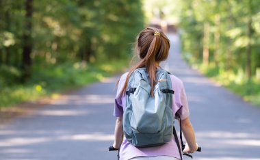 Redhead girl rides a bicycle in a beautiful summer forest. Young woman travels by bike.