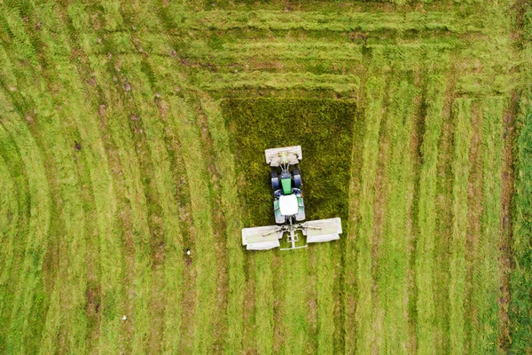 An aerial of a tractor mowing a lush grassland in summer in rural Estonia, Northern Europe.