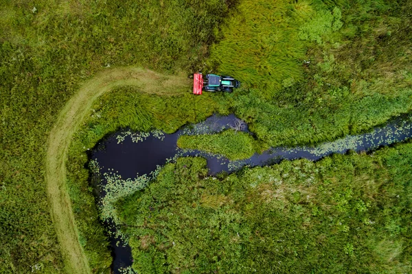 An aerial of a tractor making hay bales out of neat columns in summer grassland to make hay, Estonia.