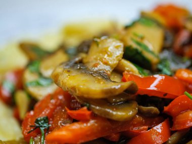 Kızarmış mantarlar ve kırmızı biberler kremalı patates püresi yatağında sunuluyor doyurucu ve rahatlatıcı bir vejetaryen yemeği sunuyor..