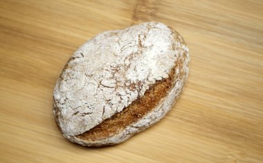 Bambu bir tahtanın üzerinde, sağlıklı bir aile kahvaltısı için hazırlanan kabuğun şeklini ve dokusunu vurgulayan bir ekşi ekmek rulosu..