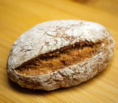 Ahşap bir yüzeyde kıtır kıtır ekşi ekmeğin yakın görüntüsü. Dokulu kabuğu ve yumuşak iç kısımları besin değeri yüksek bir aile yemeği için mükemmel aydınlatıyor..