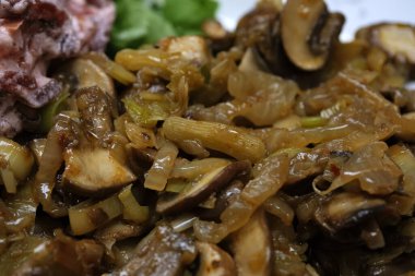 Pirzola ve soğanla pişirilmiş sotelenmiş mantar tabağı lezzetli bir vejetaryen yemeği sunuyor..