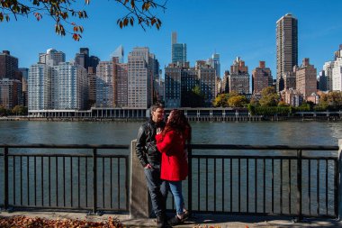 Arka planda New York binaları olan çift Roosevelt Adası 'nda yürüyor.