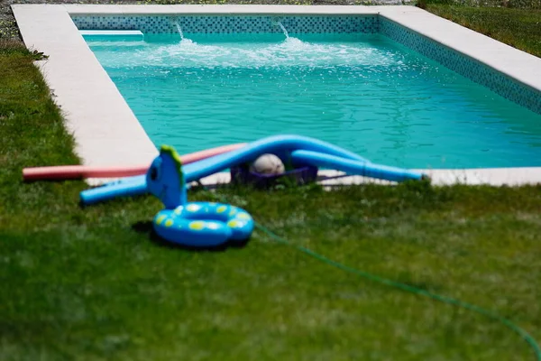 Pool filling with water without people. Floats on the grass drying in the sun