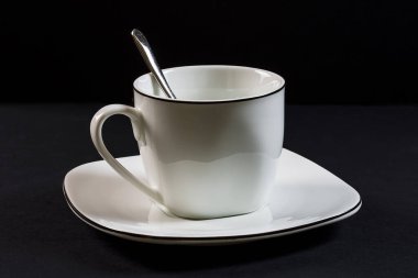 Siyah arka planda porselen bardak, kaşık ve plaka. Fotoğraf, yapay ışık olan bir stüdyoda çekilen yatay bir fotoğraf..