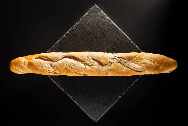 Loaf of artisan bread on a black slate.It is a still life with a black background and a zenithal point of view.The photo is taken in horizontal format.