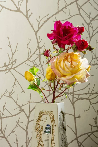Photo of a vase of natural flowers with a red rose and a yellow rose on a brown paper background.The photo is intended to be a natural image and is taken in vertical format.