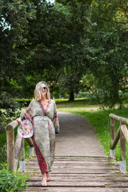 Asturias, İspanya 'daki bir parkta, tahta bir köprünün üzerinde uzun yeşil bir elbise giymiş sarışın kız. Fotoğraf dikey formatta çekilmiş..